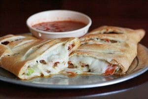 A calzone cut in two with marinara dipping sauce